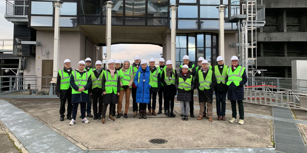 Gruppenfoto der Besucherinnen und Besucher mit Schutzhelmen und Warnwesten am Wasserkraftwerk Kembs