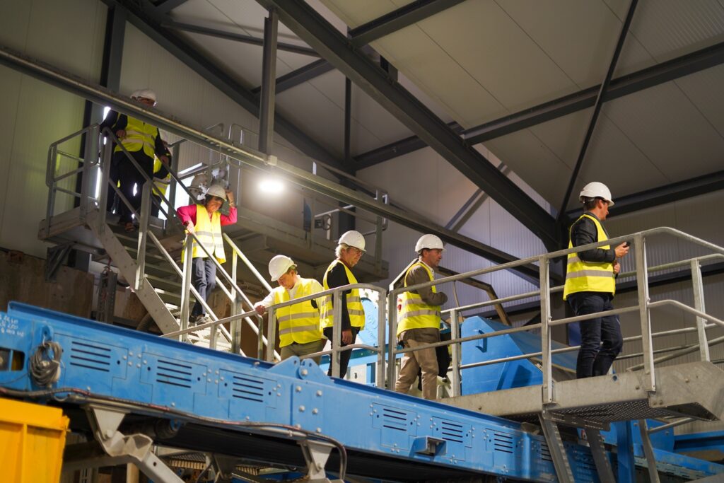 Besucherinnen und Besucher mit Schutzausrüstung auf Treppen und Stegen der Aufbereitungsanlage der habö AG