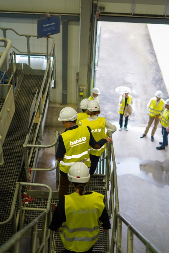 Besucherinnen und Besucher in Warnwesten steigen eine Treppe in der Halle der habö AG hinab